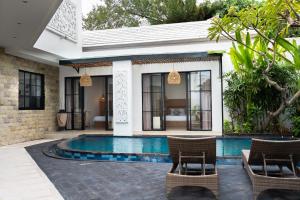 een villa met een zwembad en 2 stoelen bij Awila Villas Kuta by The Wina Resorts in Legian