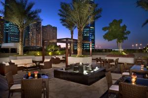 a rooftop patio with tables and chairs and palm trees at Atana Hotel in Dubai