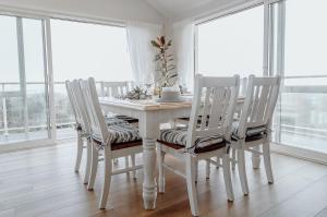 a white dining room table with white chairs and windows at Sailor's Catch in Hokitika