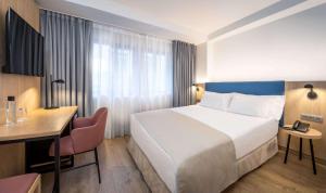 a hotel room with a white bed and a desk and a desk at Occidental Alicante in Alicante