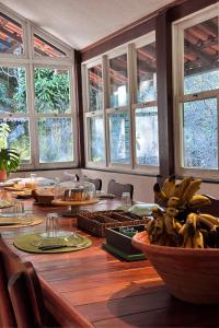 a large wooden table with bananas in a room with windows at Casa na Serra para 14 Pessoas com Piscina e Churrasqueira - Da Francesa in Bom Jardim