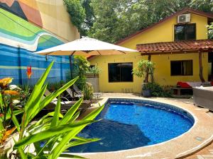 a swimming pool with an umbrella and a house at Tamarindo Backpackers in Tamarindo