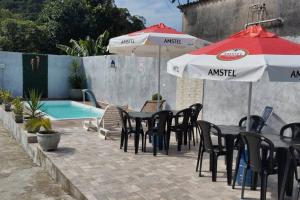 a patio with tables and umbrellas next to a pool at Casa do Barney Enseada Guaruja in Ilha de Santo Amaro