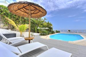 un patio con ombrellone e sedie e una piscina di Villa Vénus - classée 4 étoiles - Piscine et vue mer - Saint-Gilles les Bains a L'Ermitage-Les-Bains