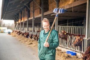 a man holding a broom in a barn with cows at Erfgoed Bossem in Lattrop