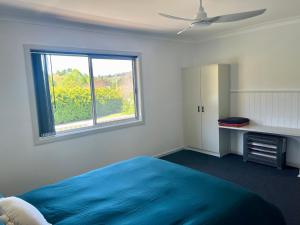 a bedroom with a blue bed and a window at Cedarvale Cottage in Boambee