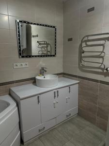 een badkamer met een witte wastafel en een spiegel bij 2 ком люкс в центре города in Karagandy