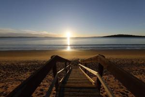 a stairway leading to the beach with the sun in the background at Beach Holiday Home-Close to Airport-3 Bed & 2 Bath in Lauderdale