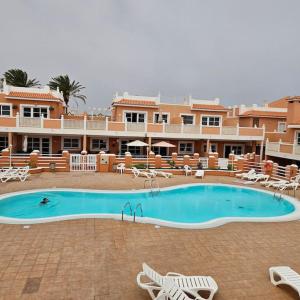 Una gran piscina con sillas y un hotel. en Esmeralda Sunny Relax, en Caleta de Fuste