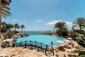a large swimming pool with palm trees and the ocean at R2 Rio Calma in Costa Calma