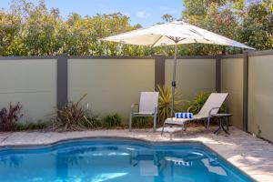 a patio with two chairs and an umbrella next to a pool at Hunter Gateway Motel in Maitland