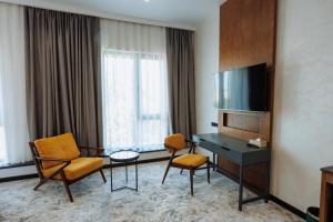 a hotel room with a desk and chairs and a television at Aurum Garden Hotel in Shymkent