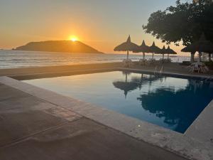 a swimming pool with umbrellas and the ocean at sunset at Islas del Sol in Mazatlán