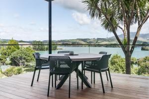 a table and chairs on a deck with a view of the water at On Point House, Luxury design, Water Views in Raglan