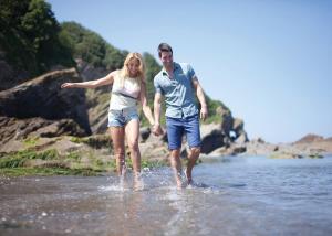 un hombre y una mujer caminando en el agua en Beach Cove Coastal Retreat, en Ilfracombe
