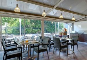 a dining room with tables and chairs and windows at B&B HOTEL Montbéliard-Sochaux in Sochaux