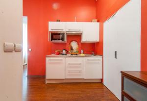 a kitchen with white cabinets and an orange wall at Piterstay Apartments - Saint Petersburg in Saint Petersburg