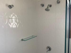 a white bathroom with a shower with a glass shelf at Pousada dos Pássaros in Gramado