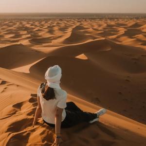 a woman sitting in the desert watching the sunset at Sahara Bedouin camp in Mhamid +28 photos
