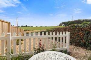 a white fence with a white bench in front of a field at Cottage On The Common in Great Malvern