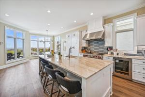 a kitchen with white cabinets and a large island with bar chairs at 4 Collier Beach Rd- Oceanfront, Private Pool, Elevator, FREE Activities Included in Hilton Head Island
