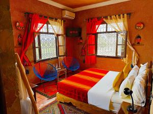 a bedroom with a bed and two chairs and windows at Riad Chay & Boutique in Ouarzazate