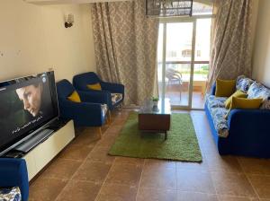 a living room with blue couches and a flat screen tv at Blumar El sokhna in Al Ḩafāʼir
