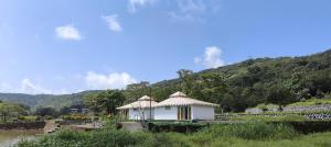 a small white building with a roof next to a river at The Purple County - Homestay in Lonavala