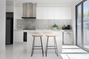 a kitchen with white cabinets and two bar stools at Modern Townhouse - Cafes, Shops, Bus, Freeway access in Balwyn North