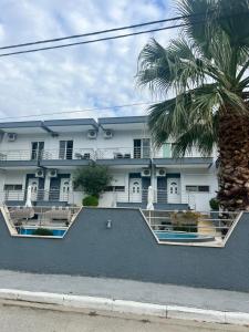 a white building with a palm tree in front of it at Family Rooms in Stavros