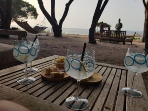 drei Weingläser sitzen auf einem Holztisch mit Essen in der Unterkunft Casa prima fila con Vista Mare in Isola Rossa