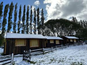 a couple of wooden cabins in a snow covered field at TRAVELLERS Camping & Dorms in San Martín de los Andes