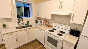 La cuisine est équipée de placards blancs et d'un four avec plaques de cuisson blanches. dans l'établissement New 1 bedroom suite North Vancouver, à Lynn Creek