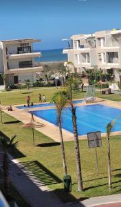 a swimming pool with palm trees in front of a building at Appart à Malaga Beach Mansouria in Mansouria
