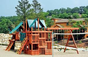a playground with wooden play equipment in front of a house at Sooner Settle Lodge 4 King Rooms Stonebridge in Reeds Spring