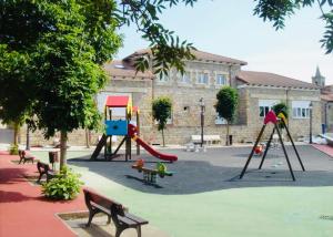 Un parque infantil con columpios y bancos frente a un edificio. en La Regalía de Requejo, en Reinosa