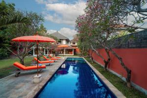 a swimming pool with orange chairs and an umbrella at Seminyak Villa Kubuku in Seminyak