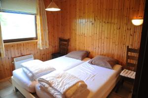 two beds in a room with wooden walls and a window at Mare aux Saules in Hotton