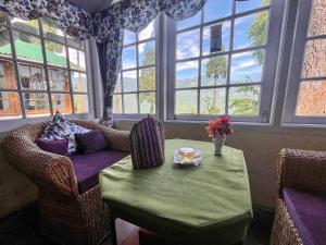 a living room with a table and chairs and windows at Yule Tea Retreat, Darjeeling in Sukhia Pokhari