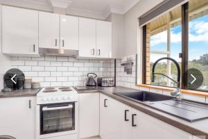 Una cocina con gabinetes blancos y un fregadero y una ventana. en Cobbers Rest, en Jindabyne