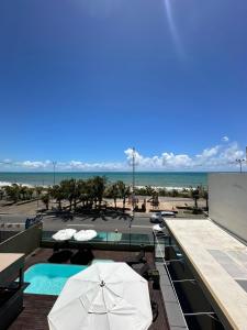 a swimming pool with an umbrella and the beach at Aloha Pousada Maceió in Maceió