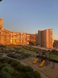 Un parque con un área de juegos con bancos y edificios amarillos. en Apt Costa de Montemar, Concón, en Concón