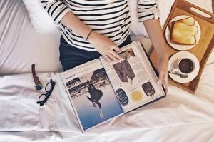 a woman sitting on a bed reading a book at My Studio Hotel Losari Makassar in Makassar