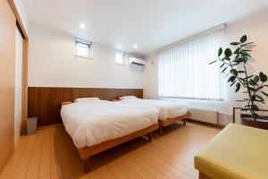 two beds in a room with white walls and wooden floors at The Casa Azucena in Sapporo