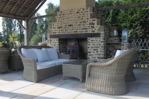 a patio with wicker chairs and a stone fireplace at Le Gîte De Roseraie in Brécé