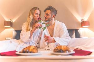 a man and woman sitting in a bed with food at Hotel Terme Salvarola in Sassuolo