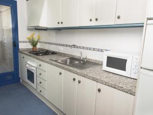 a kitchen with white cabinets and a sink and a microwave at Turquesa Beach Unitursa in Calpe