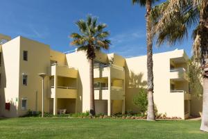 a building with palm trees in front of it at Parque Mourabel, Oásis Village & Pé do Lago in Vilamoura
