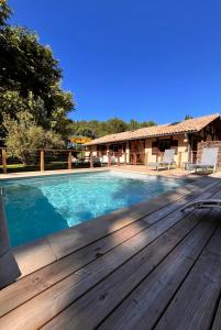 a swimming pool with a wooden deck next to a house at La bergerie des Landes in Lit-et-Mixe