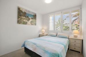 a white bedroom with a bed and two night stands at Monterey Lodge Unit 17, 27 Warne Tce Kings Beach in Caloundra